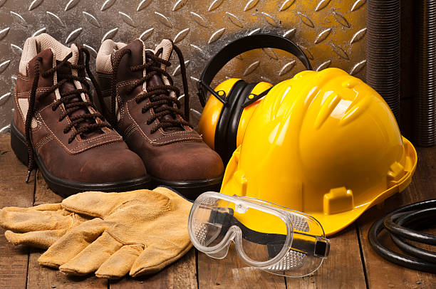 Personal protective workwear on the floor Personal Protective Workwear Shoot on Work Location. The Safety items are placed on rustic wood and includes a Yellow Hard Hat, Gloves, Steel Toe Shoes, Ear Muff and Goggles. A silver diamondplate in the background. Predominant colors are yellow and brown protective workwear stock pictures, royalty-free photos & images