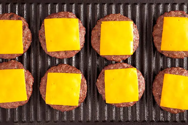 Several burgers with cheddar cheese slices over them