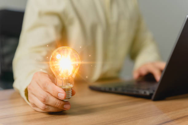 istock Man holding a light bulb while working on a computer laptop to think and generate new ideas through technological innovation and creativity. Idea inspired by online technology and innovation. 1549374352