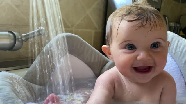 Baby plays and splashes in the kitchen sink while taking a bath