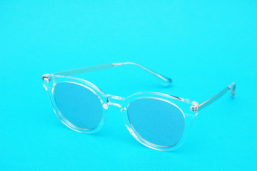 Toned image of glasses. Sunglasses with a transparent frame and blue lenses on a blue paper background.