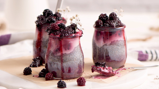 Chia pudding with blackberries, three portions in glass jars on a white table.