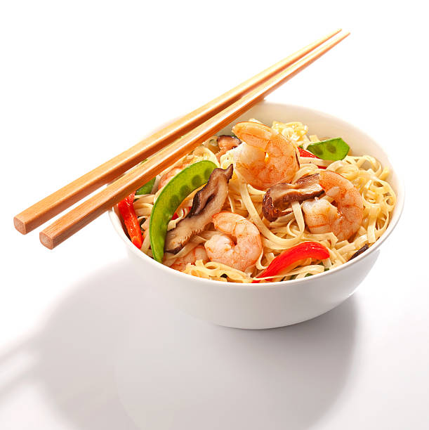 A beautifully plated dish of Pad Thai noodles topped with crispy fried shrimp, served with fresh bean sprouts and a side of dipping sauce on a sleek black plate. The warm lighting and dark background enhance the rich textures and vibrant colors of this classic Thai dish. Known for its balance of sweet, savory, and tangy flavors, Pad Thai is a staple of Thai street food and fine dining. This image is perfect for food photography, restaurant menus, culinary blogs, and Thai cuisine branding.