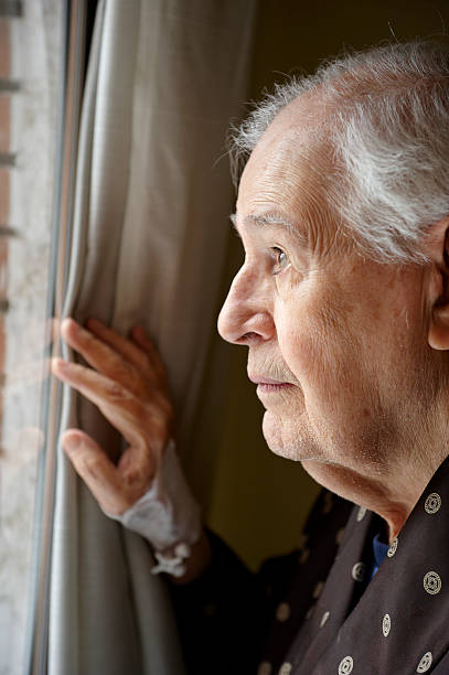 istock An elderly man peers through a window holding curtain aside  154945760