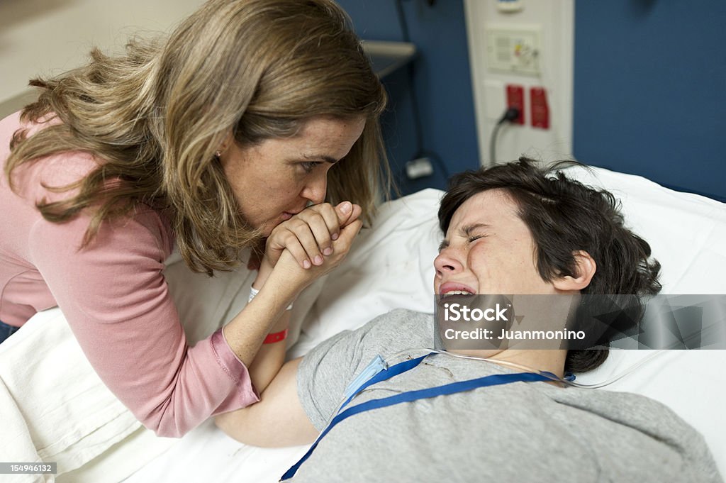 Pain at the emergency room Mature caucasian woman kissing his son hand while he is in pain at a hospital emergency room after braking his leg playing sports Child Stock Photo