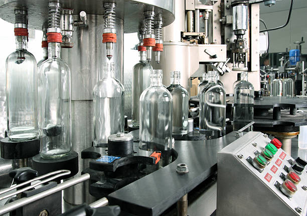 Bottling plant detail. Automated process of bottling in a small distillery.Freshly distilled gin is being filled into transparent 1 liter glass bottles. Control buttons are visible on the side of the conveyor line. bottling plant stock pictures, royalty-free photos & images