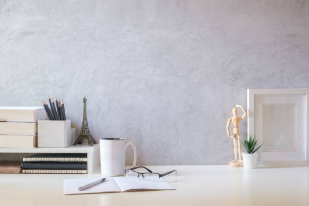 istock Bright modern workplace with flower pot, coffee cup, picture frame and books on white table. Copy space for your text. 1549464344