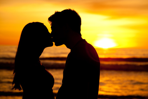 Young couple in silhouette kissing with beach sunset background.