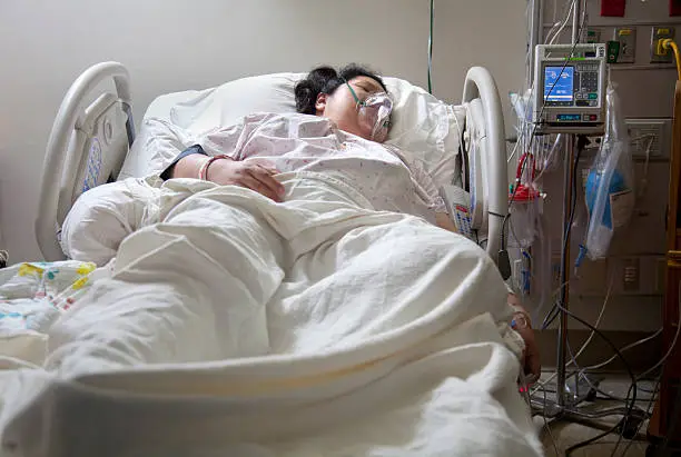An adult woman in a hospital recovery bed wearing an oxygen mask.