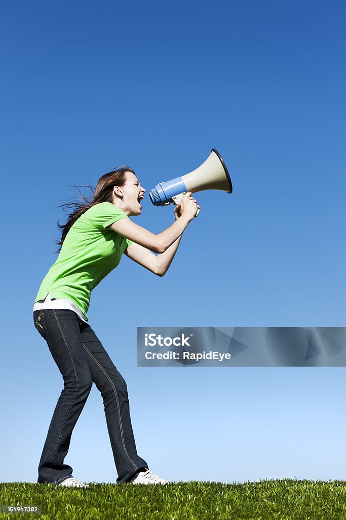 Pretty brunette yells into loud hailer against blue sky  Cut Out Stock Photo