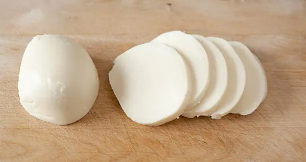 Slices of fresh mozzarella cheese on a wood cutting board.