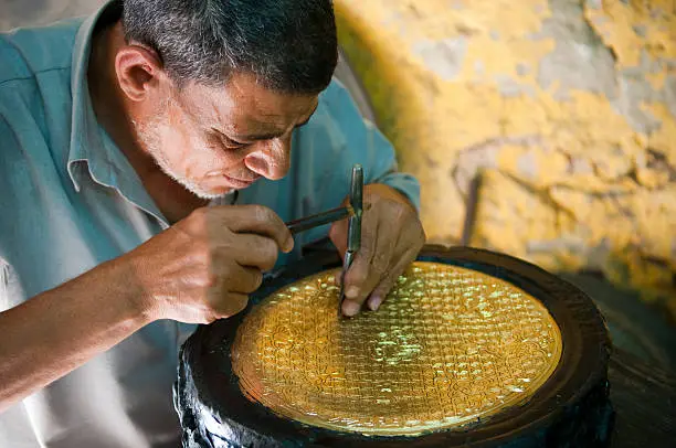 An Egyptian man at a workshop in Islamic Cairo, in a neighborhood behind the Khan el-Khalili Bazaar, chisels into a copper plate to create a beautiful design. The job will take at least two days.