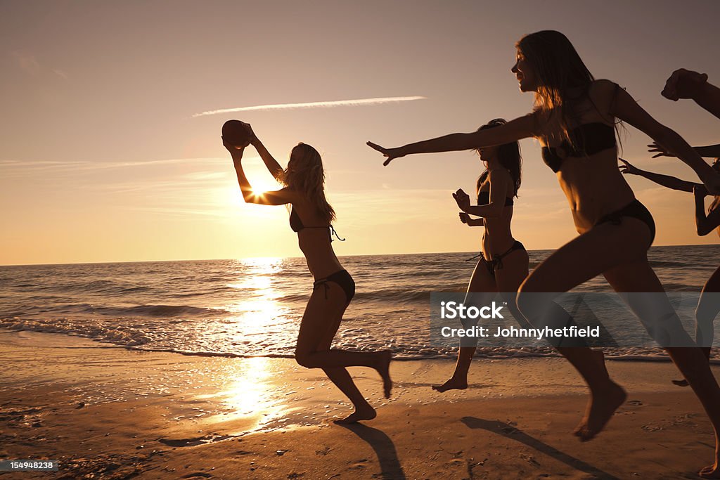 Friends playing ball at the beach Silhouetted against a beautiful sunset American Football - Sport Stock Photo