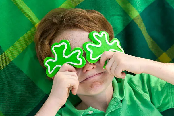 Redhead and freckle face Irish boy leprechaun with shamrock cookies over his eyes. Smiling Irish child wearing green on St. Patrick's. (SEE LIGHTBOXES BELOW for more holdiday food and people backgrounds...)