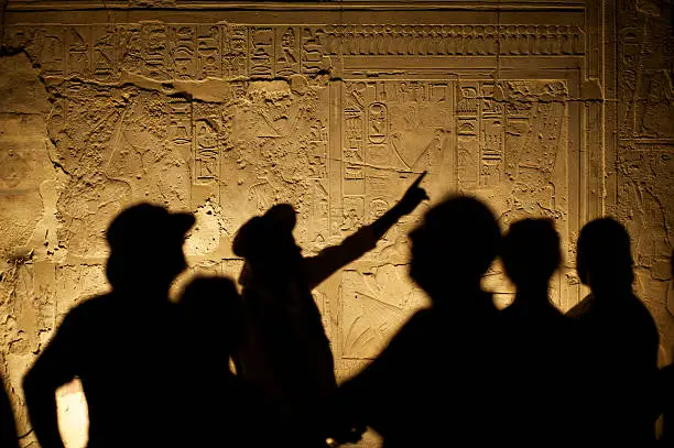 Egyptian hieroglyphs make an interesting background for silhouetted group of tourist archeologists
