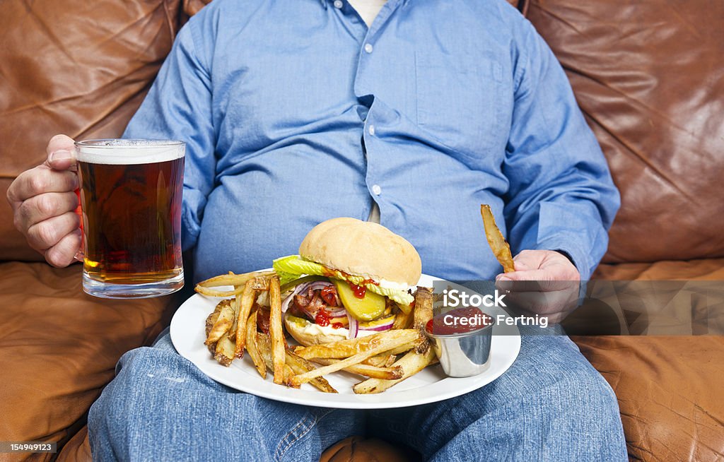 Obesity is a major cause of diabetes A photo of an overweight man sitting on an old couch with a very large unhealthy meal on his lap and a pint of beer in his hand. Obesity is a major cause of diabetes. Overweight Stock Photo