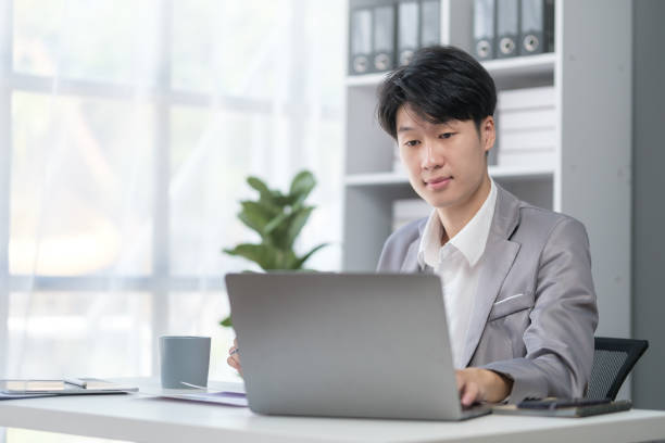 istock Businessman using laptop computer at desk in modern workplace. 1549497036