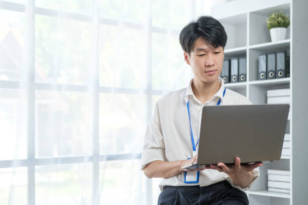 istock Handsome young asian man working on laptop computer at contemporary office. 1549498682