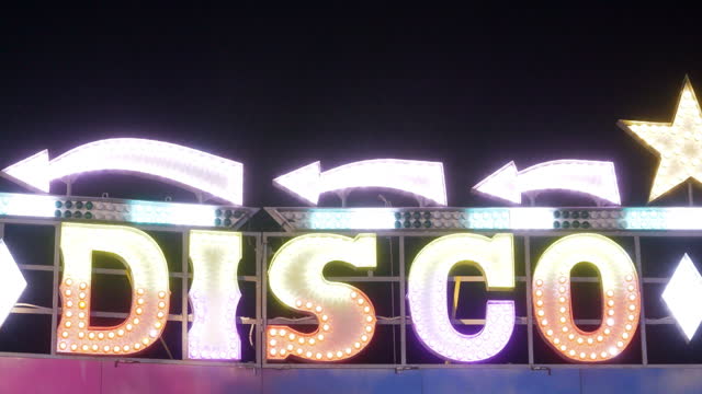 Disco sign decorated with flashing lights in amusement park at night.