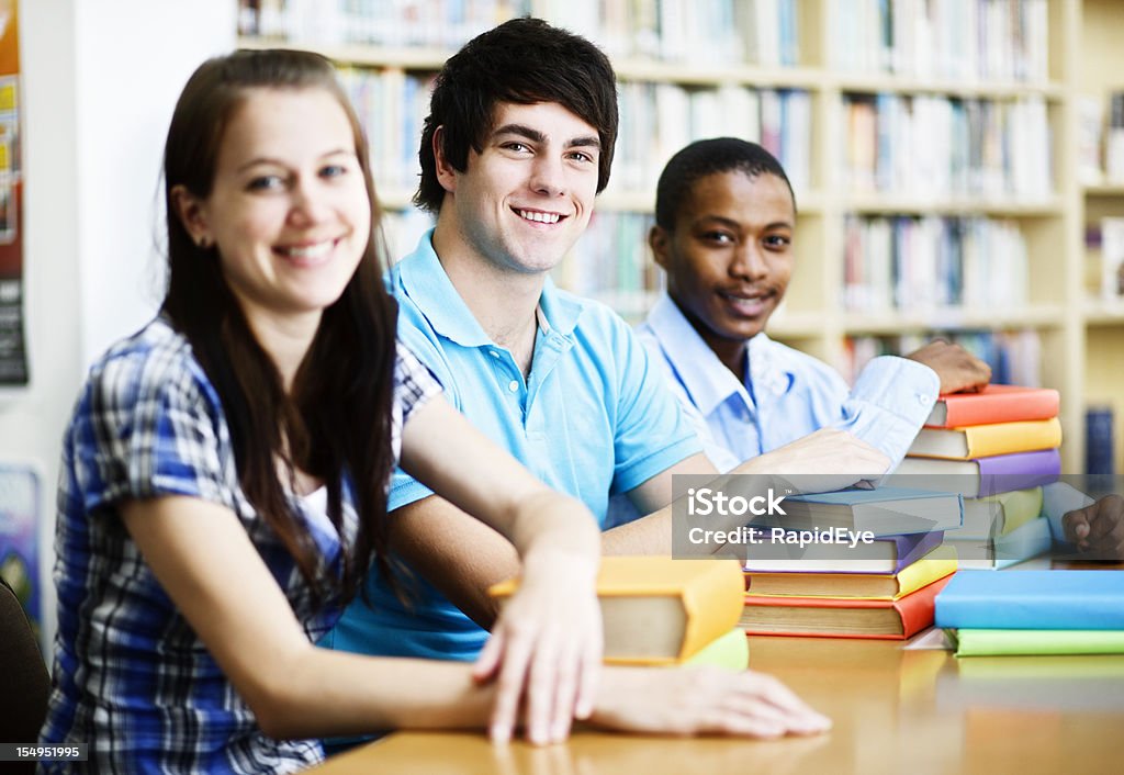 Три улыбающихся студентов Поделитесь хорошей, библиотека столом - Стоковые фото 20-29 лет роялти-фри