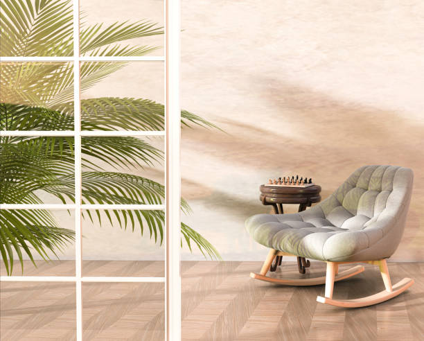 istock Small room interior with a rocking chair, a beige concrete wall, a chessboard on an decorative table, large windows, a fern tree and sunlight reflections. 1549522862