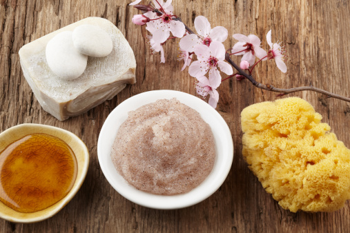 Mineral soap, sea sponge, cherry blossoms, honey and salt scrub on a distressed wood surface