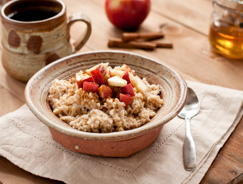 Rustic pottery bowl of steel cut oatmeal with apples, honey, and cinnamon and a cup of coffee.