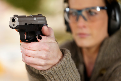 A woman pointing a gun at the camera. Focus is on the gun.