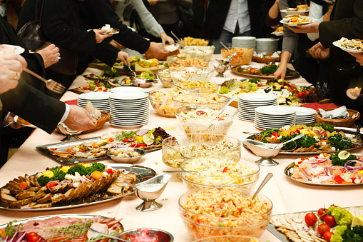 Catering table full of tasty food. Many hands of unrecognizable persons. 