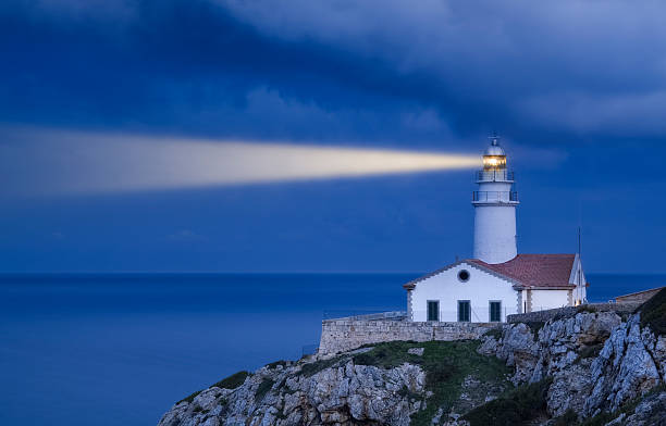 Lighthouse in Blue - Far de Capdepera Shining Lighthouse on the Cliff by Night. Far de Capdepera the easternmost point of Mallorca. rocky coastline stock pictures, royalty-free photos & images