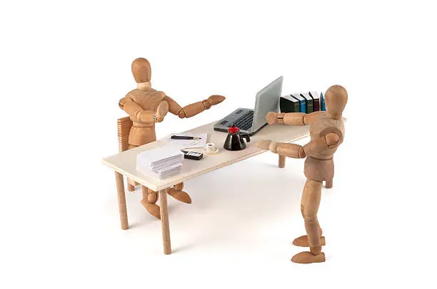 Serie of wooden mannequins in different team discussion situations. Here mannequin has a discussion with the secretary. Why? He can not go to the chef? She doesnt want to hear his problem? Clean desk with paper, coffee and handy. 