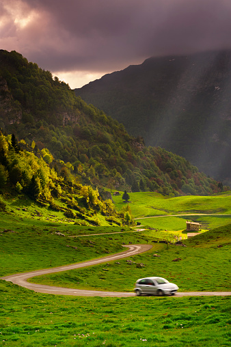 small car driving along a bendy mountain road through with sun rays beaming through. Col D'Agnes, French Pyrenees.