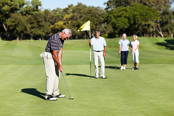 Male golfer taking his putt with man holding a flag and women watching