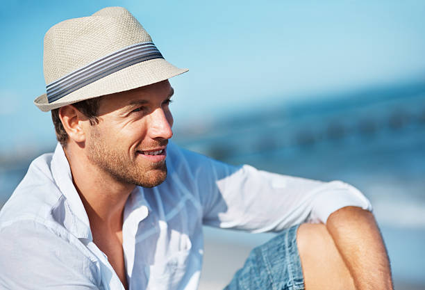 Portrait of smiling handsome man in a fedora hat relaxing on the beach