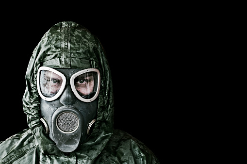 Man wearing cold war era chemical, radiation and biological protection mask and suit. Fine noise applied, Isolated on black.