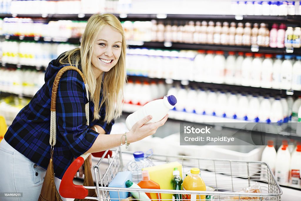 Pretty blonde shopper smilingly chooses milk from supermarket fridge  Milk Stock Photo