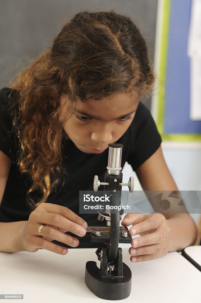 Hispanic American Girl with Microscope Learning Science Education This is a vertical color photograph of a young Hispanic, American girl learning science in elementary school. She is studying a glass slide, looking into a microscope used for education purposes. Photographed with a Nikon DSLR.  Back to School Stock Photo