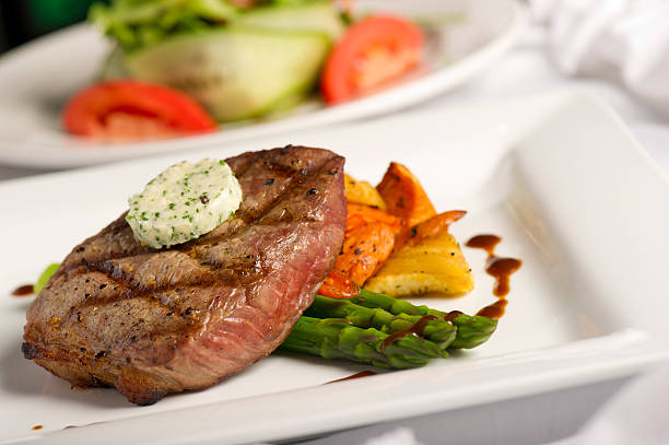 Grilled Steak with herb butter, roasted vegetables and asparagus in the foreground with a garden salad in the background
