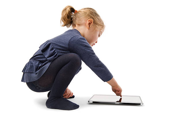 A cute three years old girl squatting,touches a tablet computer screen on white background.