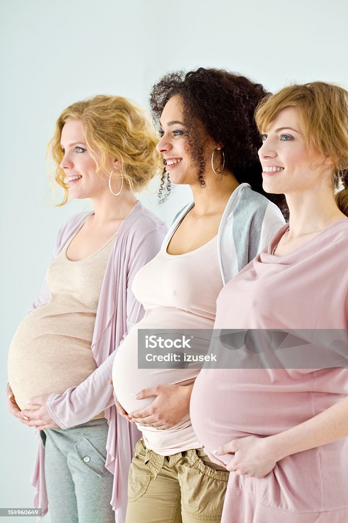 Proud pregnant women Three happy and proud, pregnant young adult women standing in a row against white background and holding their pregnant bellies. Looking in one direction. Pregnant Stock Photo