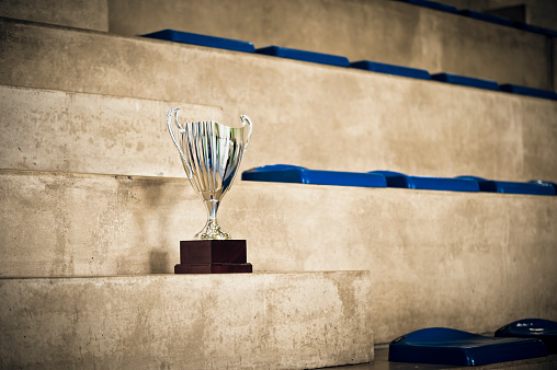 Golden trophy on top of old wooden table in front of concrete blackboard. 3d rendering.