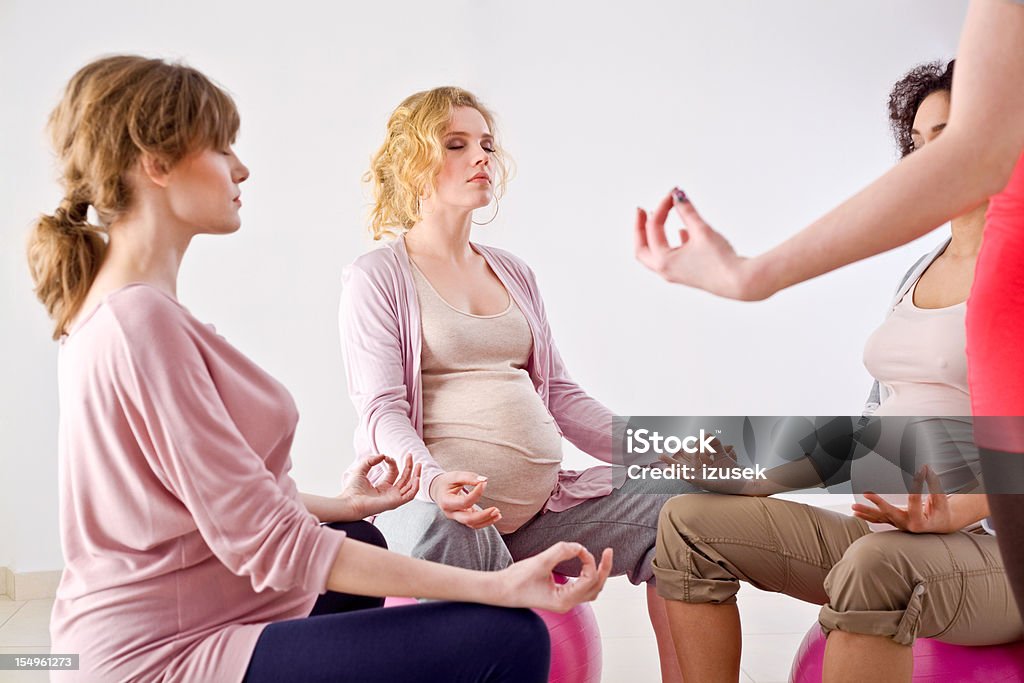 Pregnant women doing yoga Three pretty, pregnant young adult woman sitting on the gym ball and meditating with their yoga instructor. 20-24 Years Stock Photo