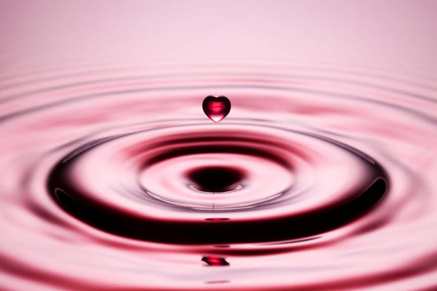Freeze frame macro photograph of a heart shaped water drop falling into red water.