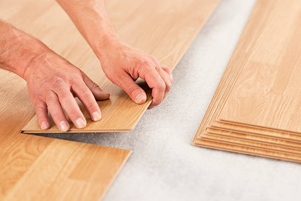 Picture of man's hands laying yellow laminate flooring Man laying laminate flooring planks. Oak effect planks being placed over insulating foam underlay. wood laminate flooring photos stock pictures, royalty-free photos & images