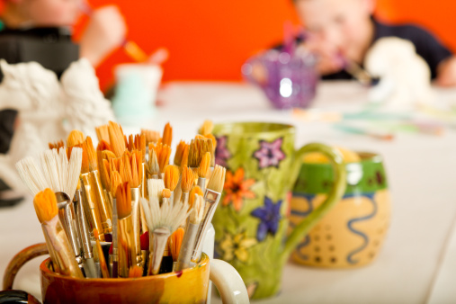 Hand painted Cup Full of Paintbrushes with children painting in the blurred background