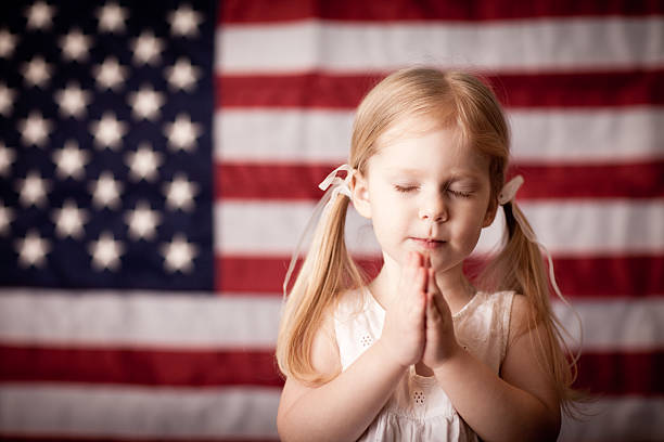 kleines mädchen beten vor amerikanischen flagge - serene people tranquil scene child god stock-fotos und bilder