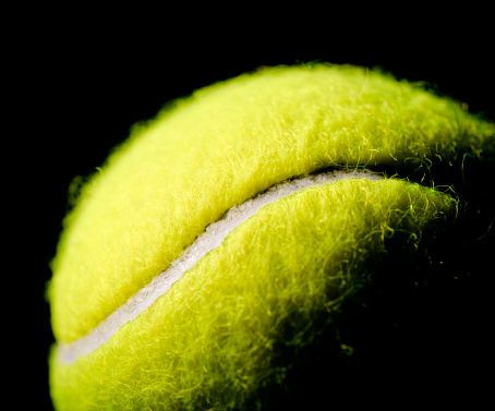 Close up on a new tennis ball against a black background.