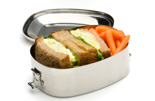 stainless steel lunch box containing an egg salad sandwich and baby carrots, on white background
