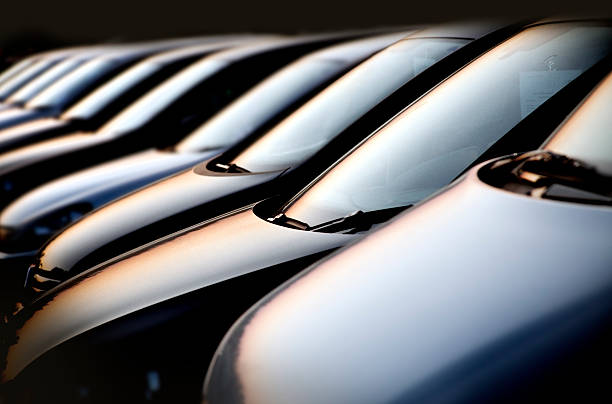Line of cars at sunset line of new black compact cars at a dealer lot at night. Focus is on the first two cars. Image has a black background. Shot was taken with full format camera and prime lens, processed in raw and was carefully retouched bmw dealership stock pictures, royalty-free photos & images