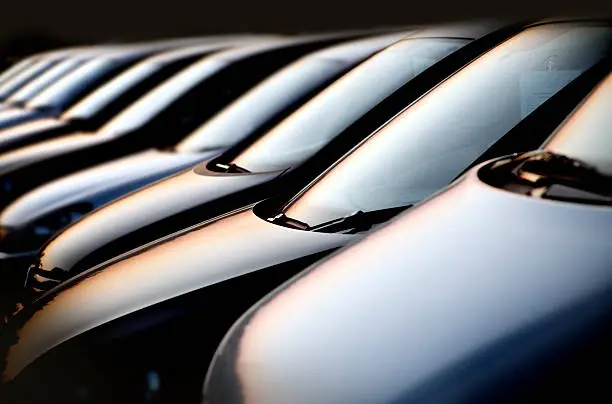 line of new black compact cars at a dealer lot at night. Focus is on the first two cars. Image has a black background. Shot was taken with full format camera and prime lens, processed in raw and was carefully retouched